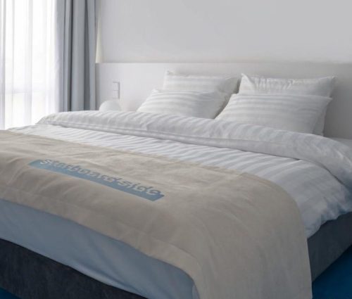 Покрывало саше с вышивкой логотипа и постельное бельё на двуспальной кровати в отеле Старборд - h-2 крупным планом.